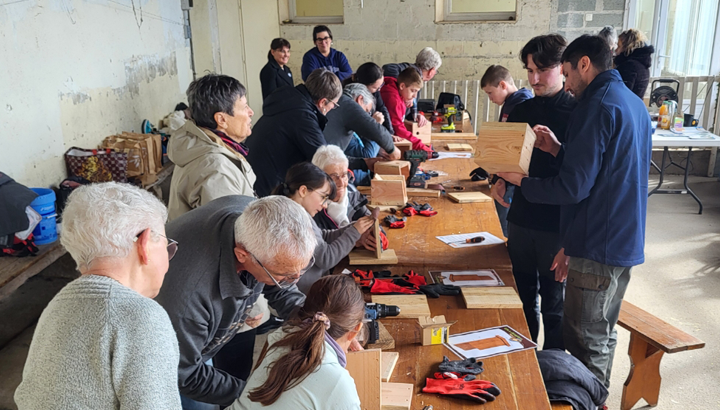 Un groupe de personne intergénérationnelle réalise des nichoirs en bois dans un atelier autour d'une table rectangulaire en bois avec la LPO